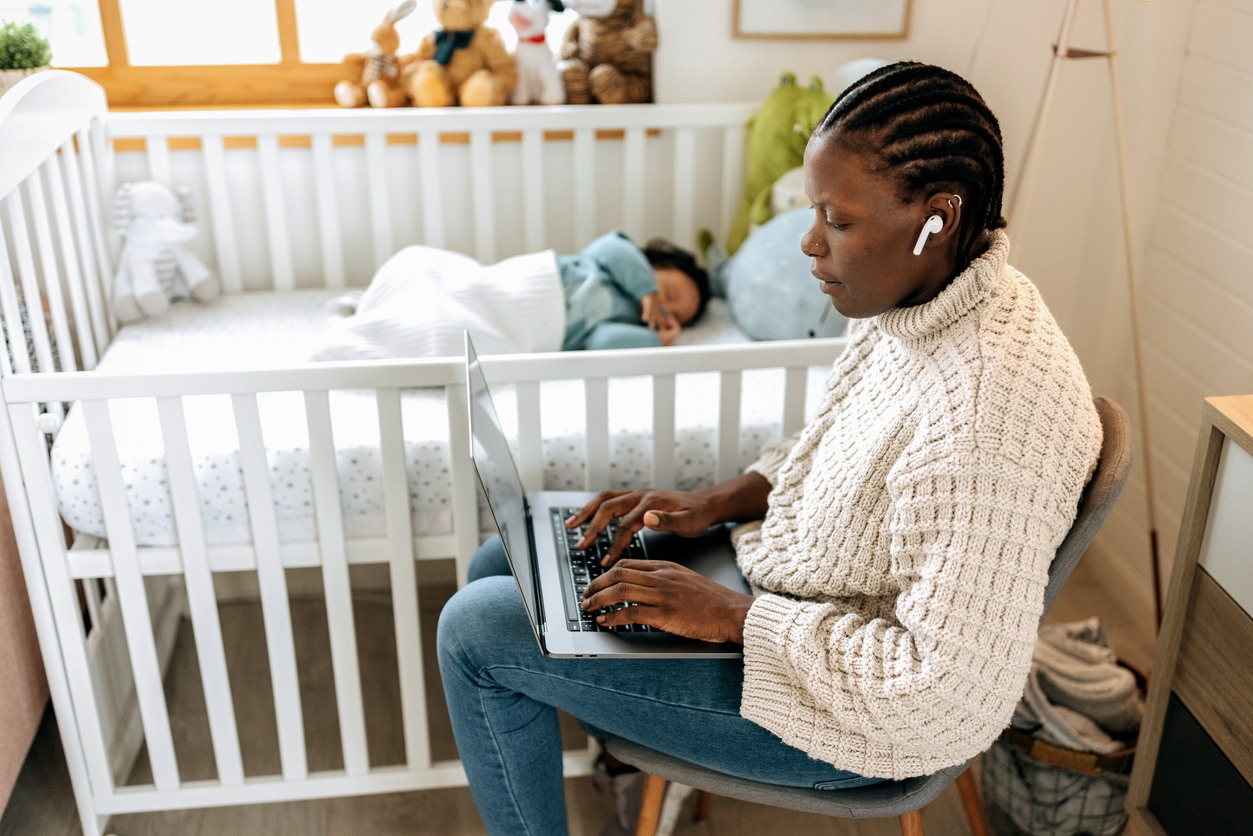 woman at a laptop, sitting next to her baby sleeping