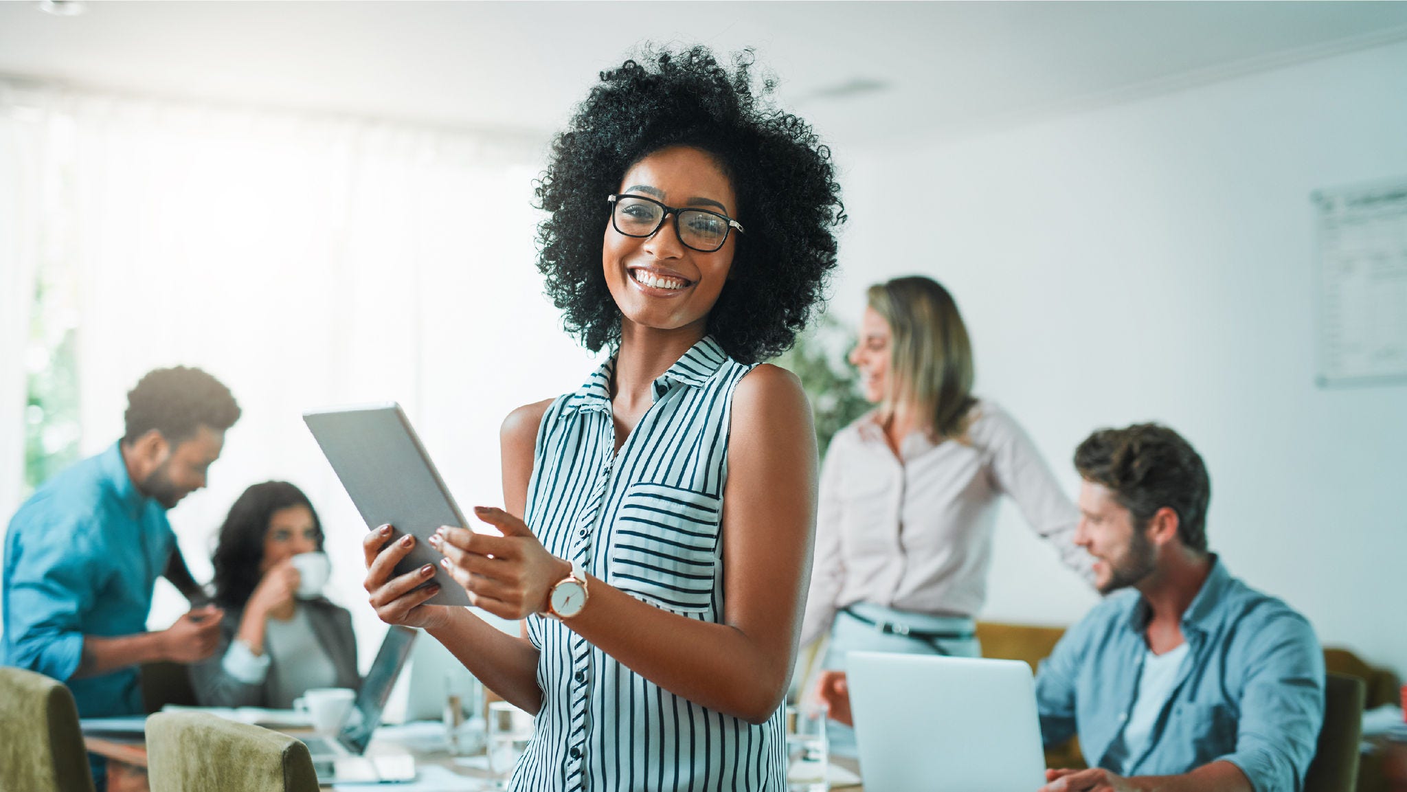 woman smiling while holding ipad in front of colleagues