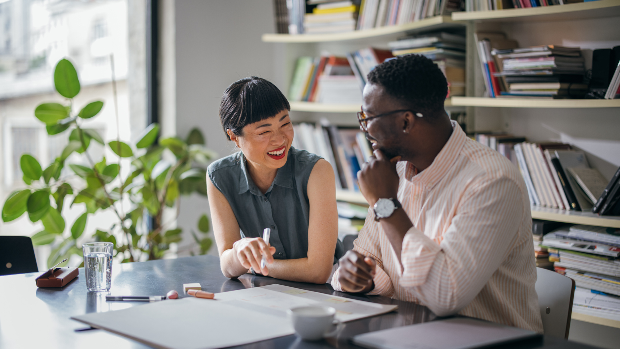 A young African American male and older asian American professional seated at a desk in a contemporary office happily working together.