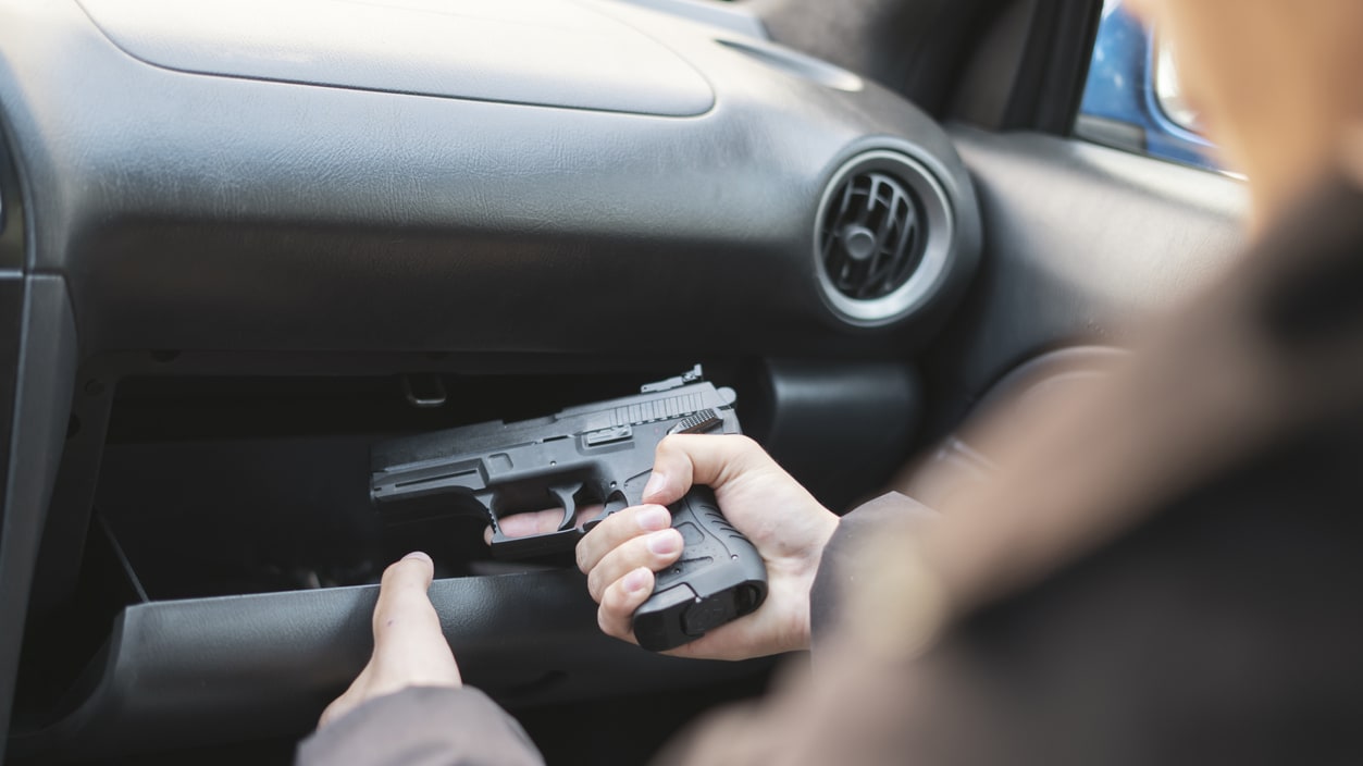 A person pulling a gun out of a car glovebox.