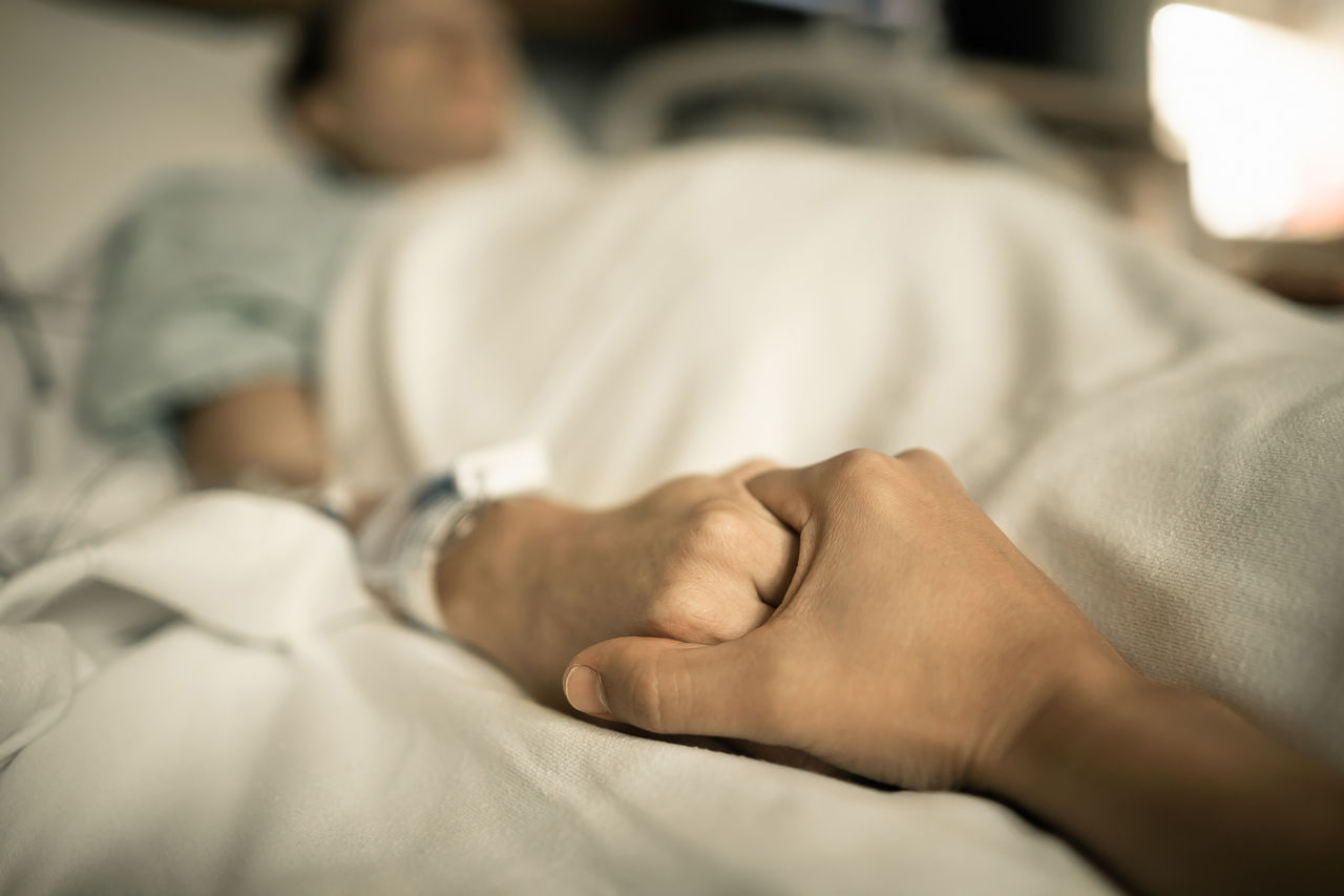 Someone holding the hand of another, giving support and comfort to spouse sick in hospital bed