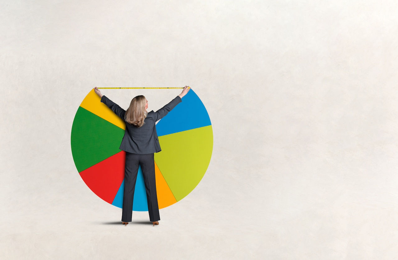 A woman raises her arms as she uses a tape measure to measure a missing piece of a pie chart.
