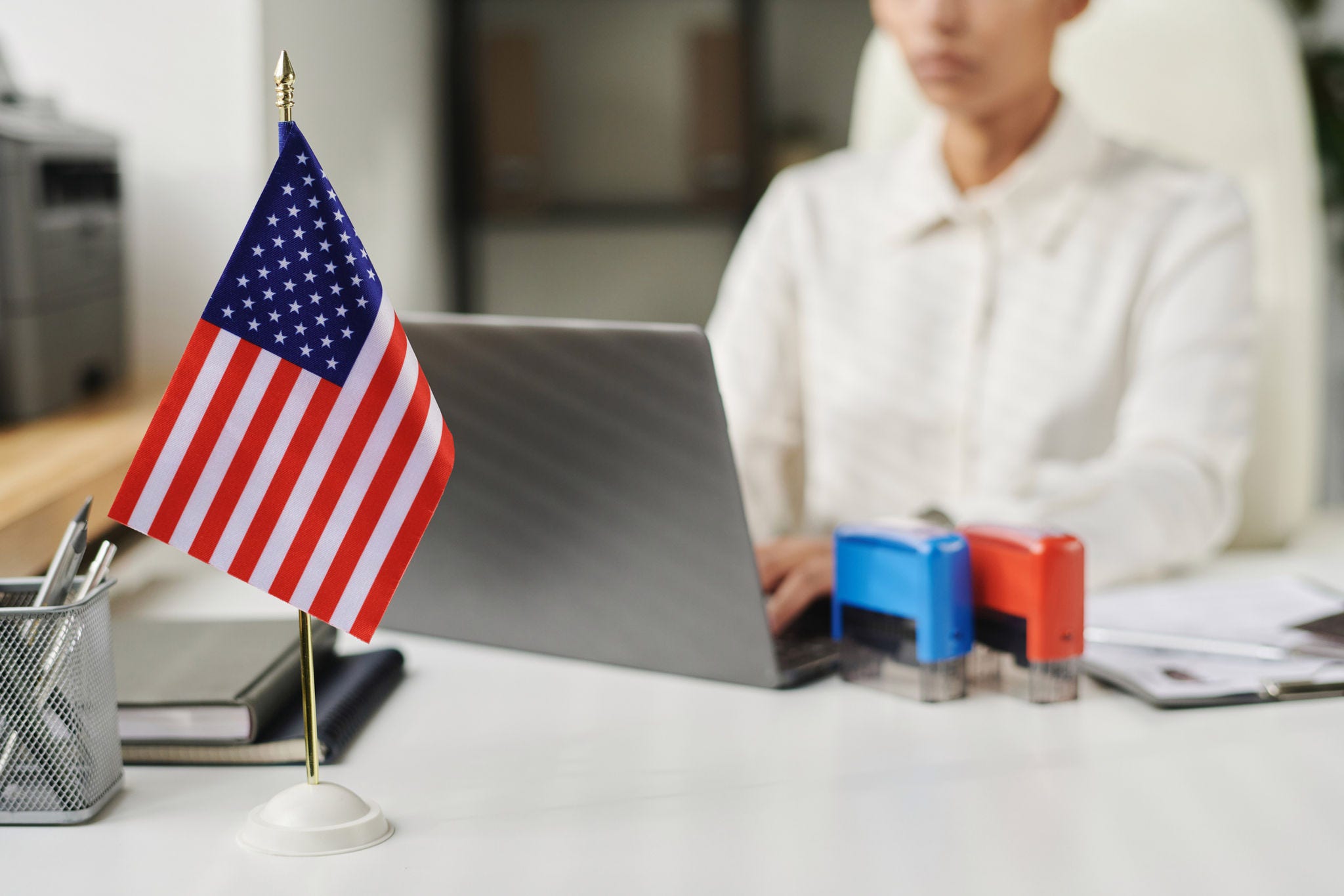 Workplace with american flag in office with visa center employee working on laptop in background