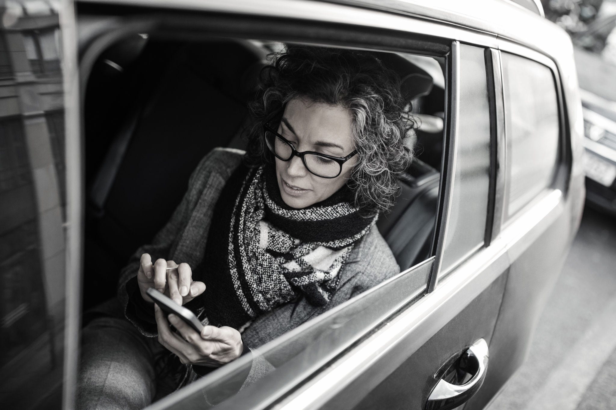 Mature woman reading text message on her cell phone while traveling by a a car. Mid adult female business professional traveling by a car and texting on her mobile phone.