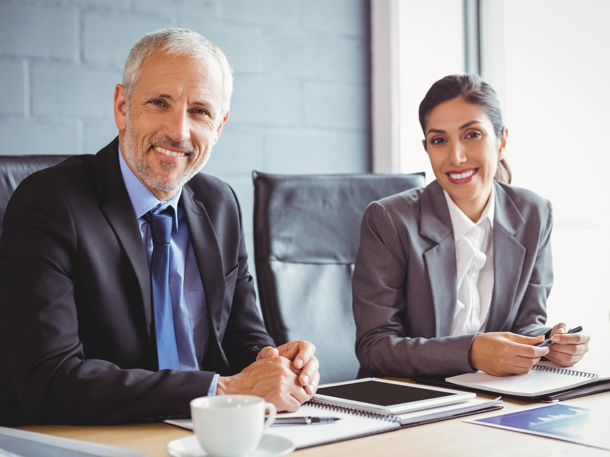 a smiling businessman and businesswoman sit next to each other at a table