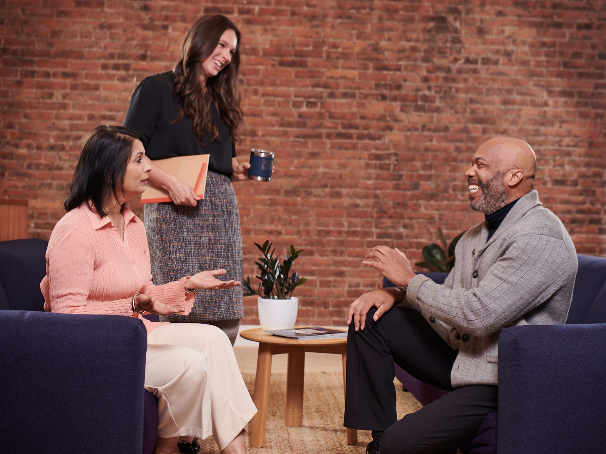 Three colleagues laugh during a meeting in an open format workspace.