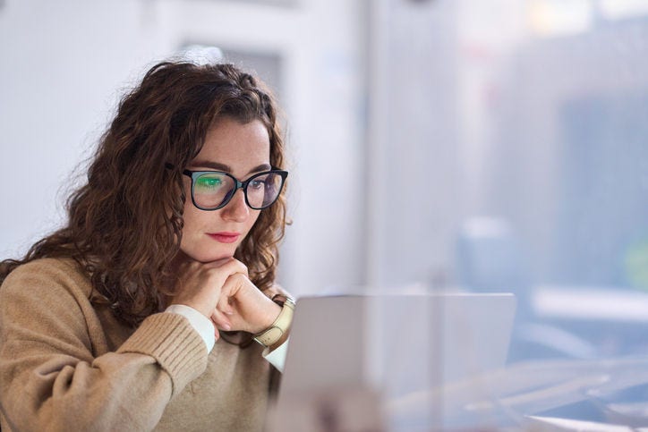 Young serious busy professional business woman employee or student wearing glasses using laptop watching online webinar or training web course, looking at computer, thinking, doing research.