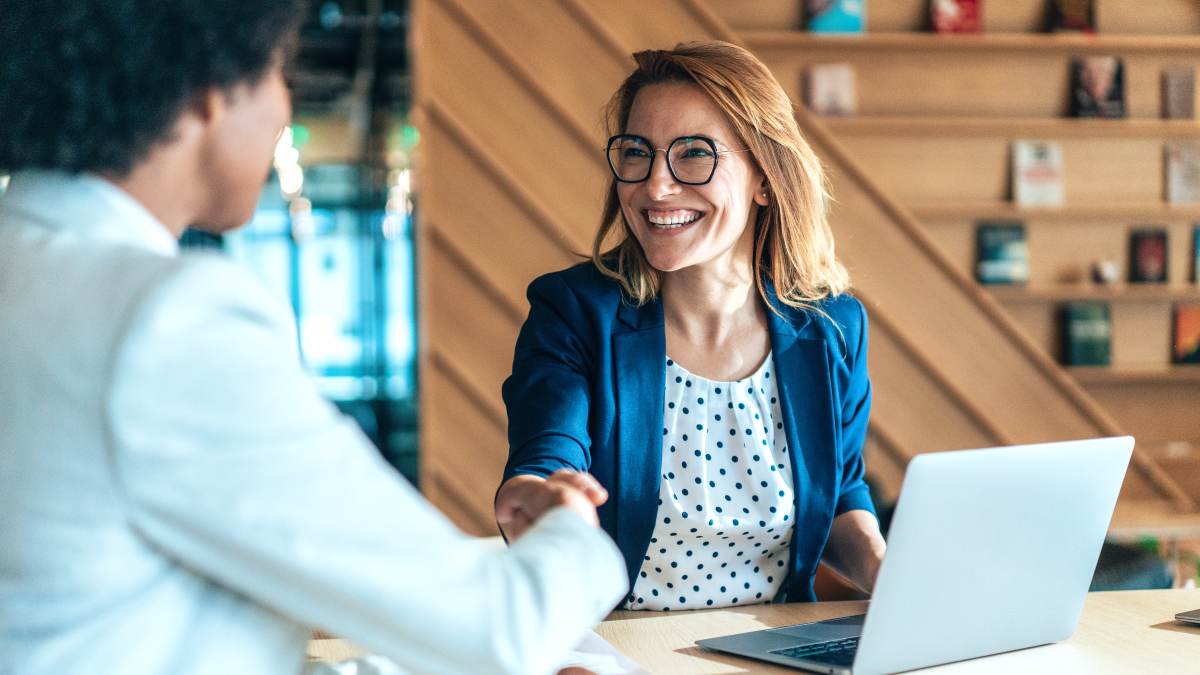 professional woman shaking hands with a man in front of a laptop