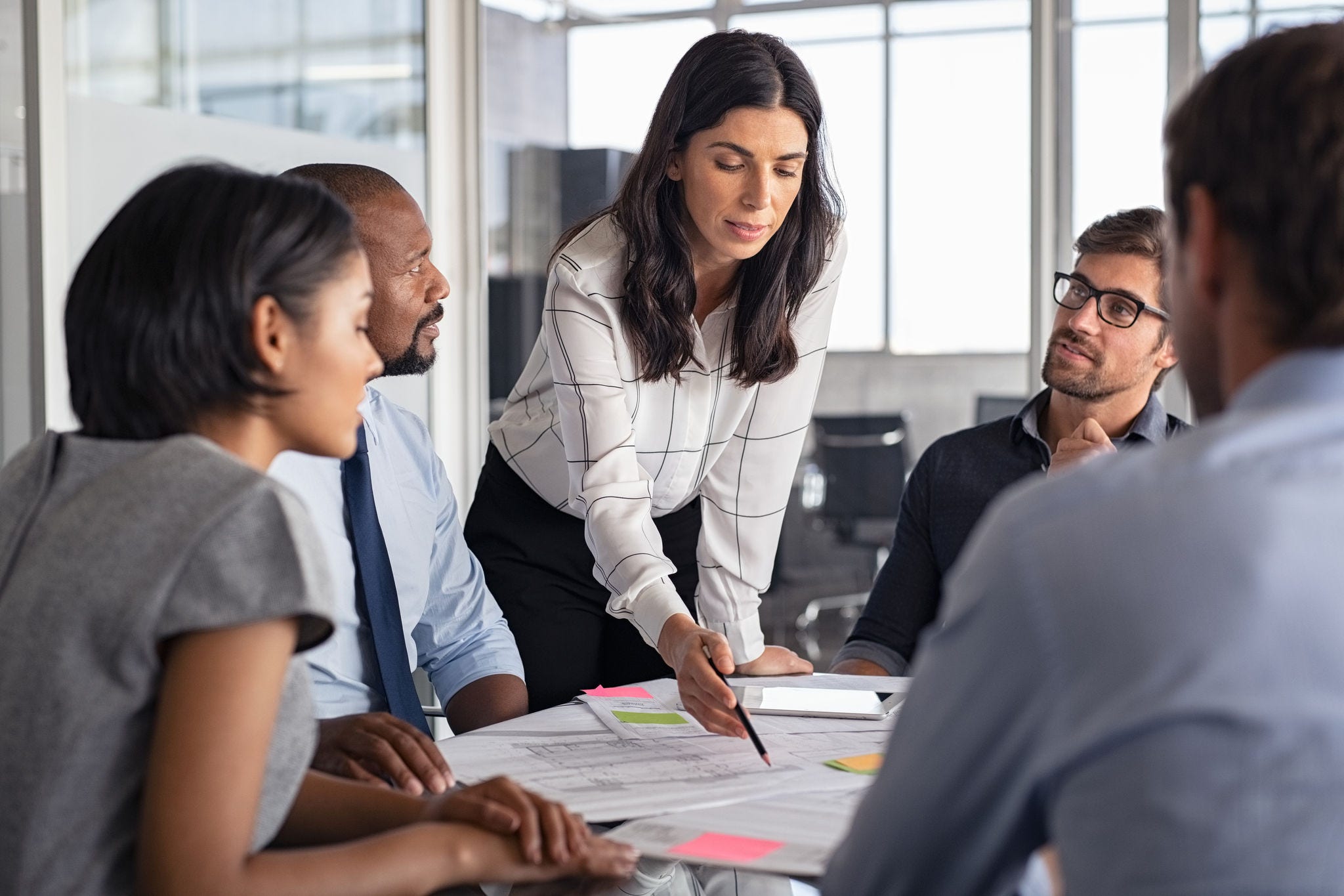 Team of multiethnic architects working on construction plans in meeting room. Engineers and designers discussing project in office. Businesswoman with business team in conference room working on blueprint.