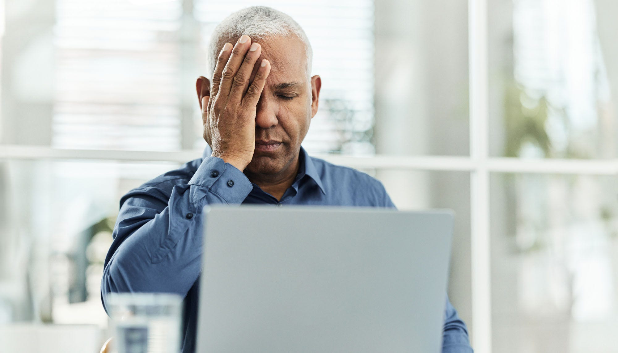 older man looking overwhelmed with hand over his face in front of laptop
