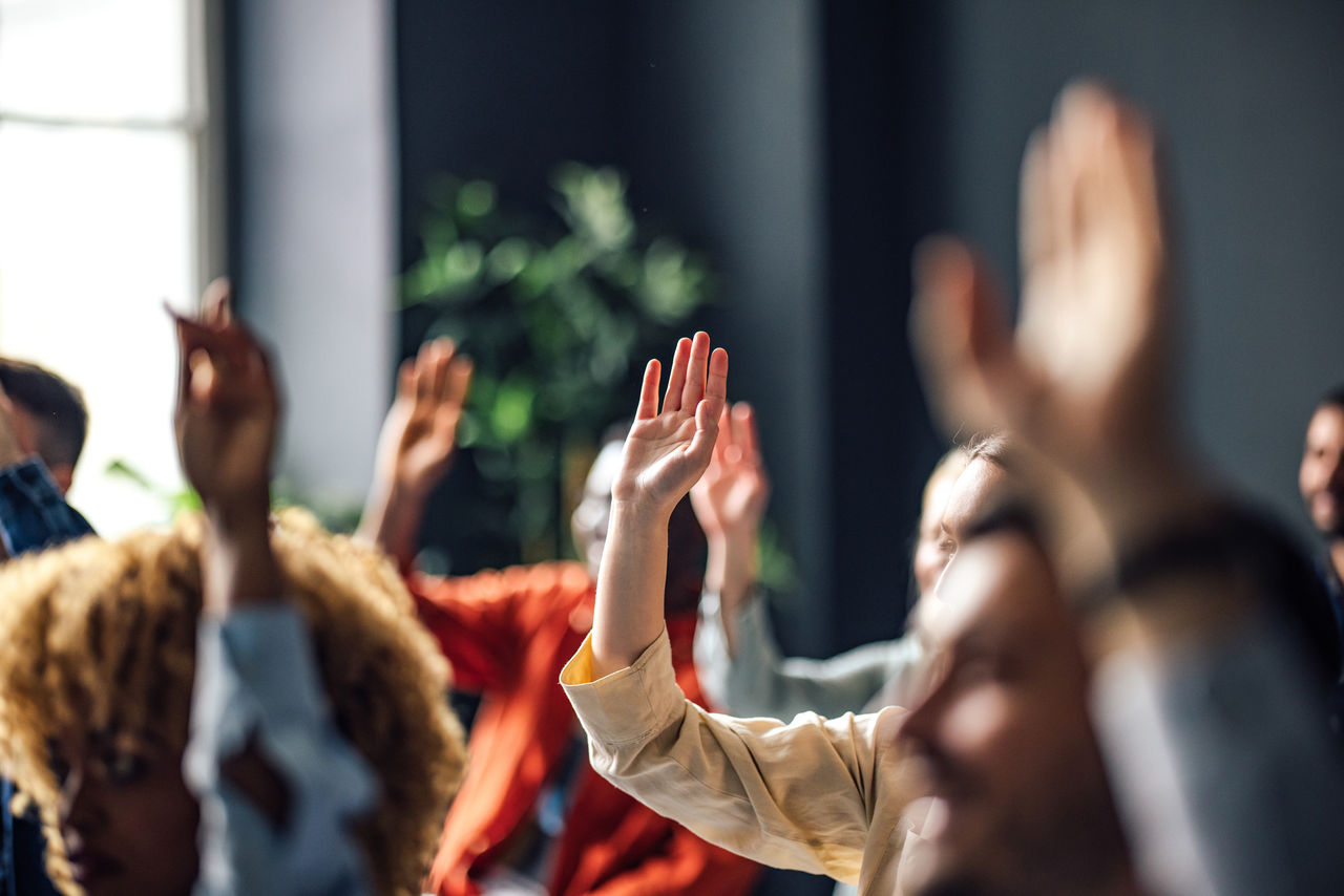 A group of people with their hands raised to ask a question.