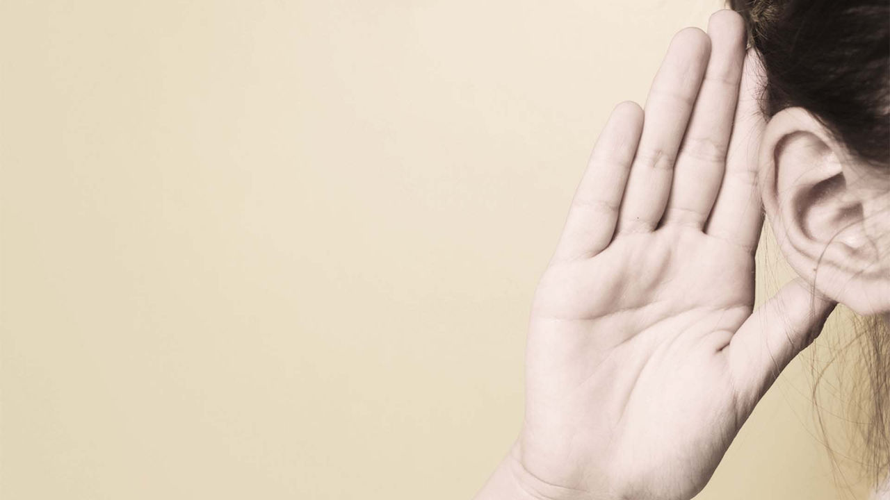 A woman is holding her hand up to her ear.
