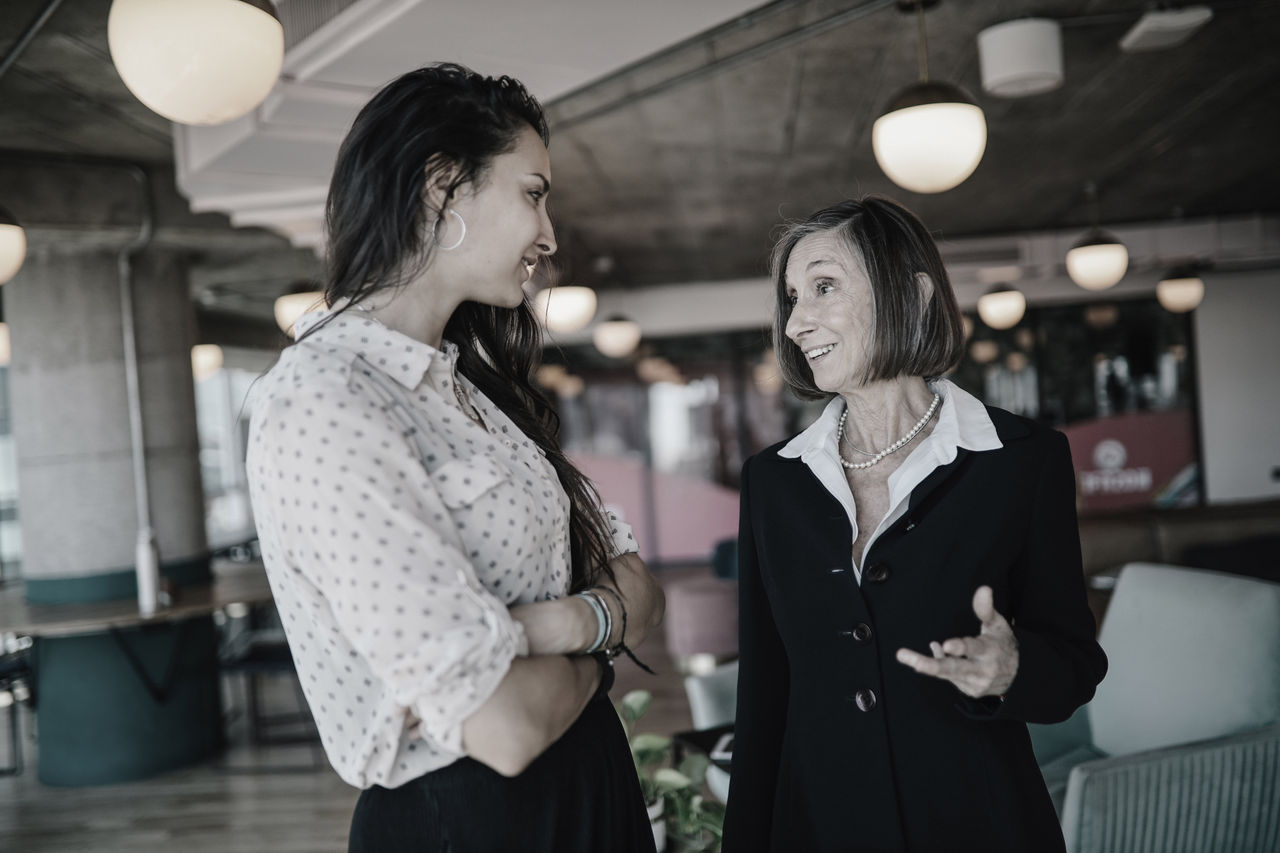 A young professional woman speaks to a senior colleague in an office.