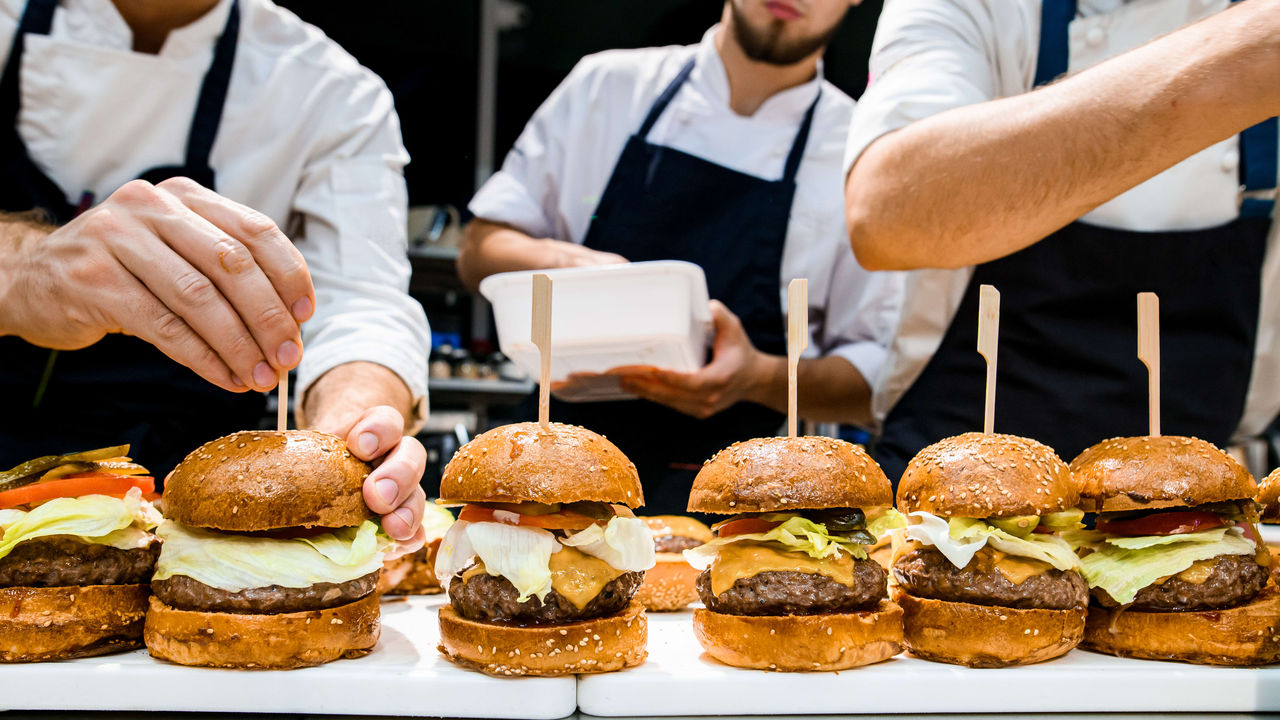 A group of chefs preparing burgers on a tray.