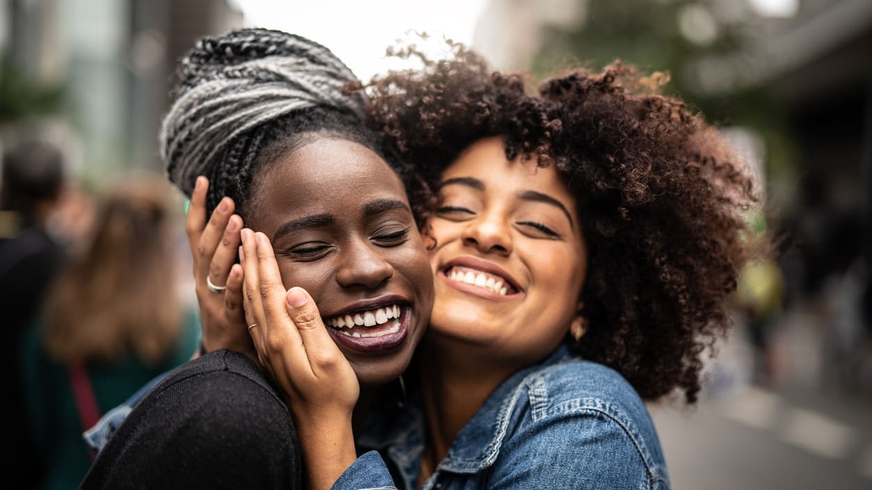 Two black women hugging each other on the street.
