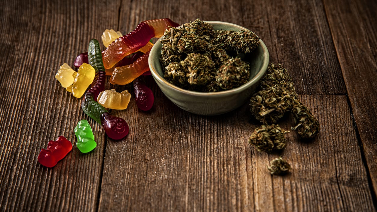 Marijuana falling out of a bowl and gummies on a table.