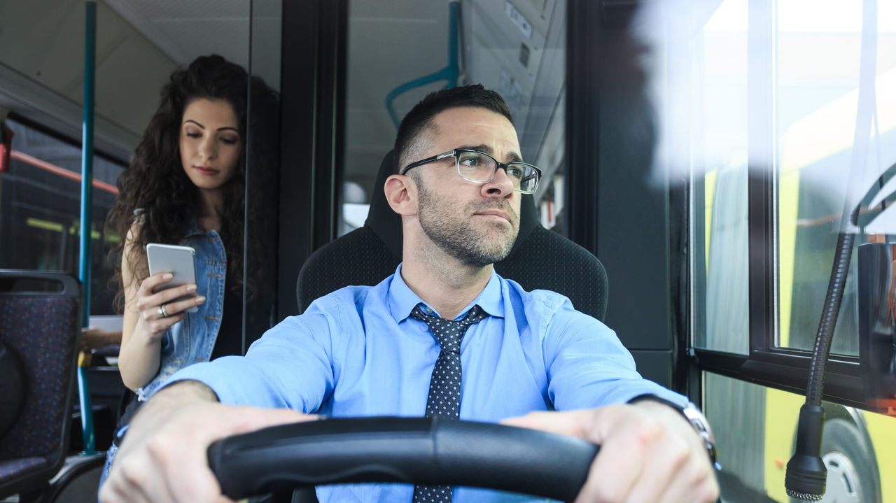A man driving a bus while a woman is looking at her phone.