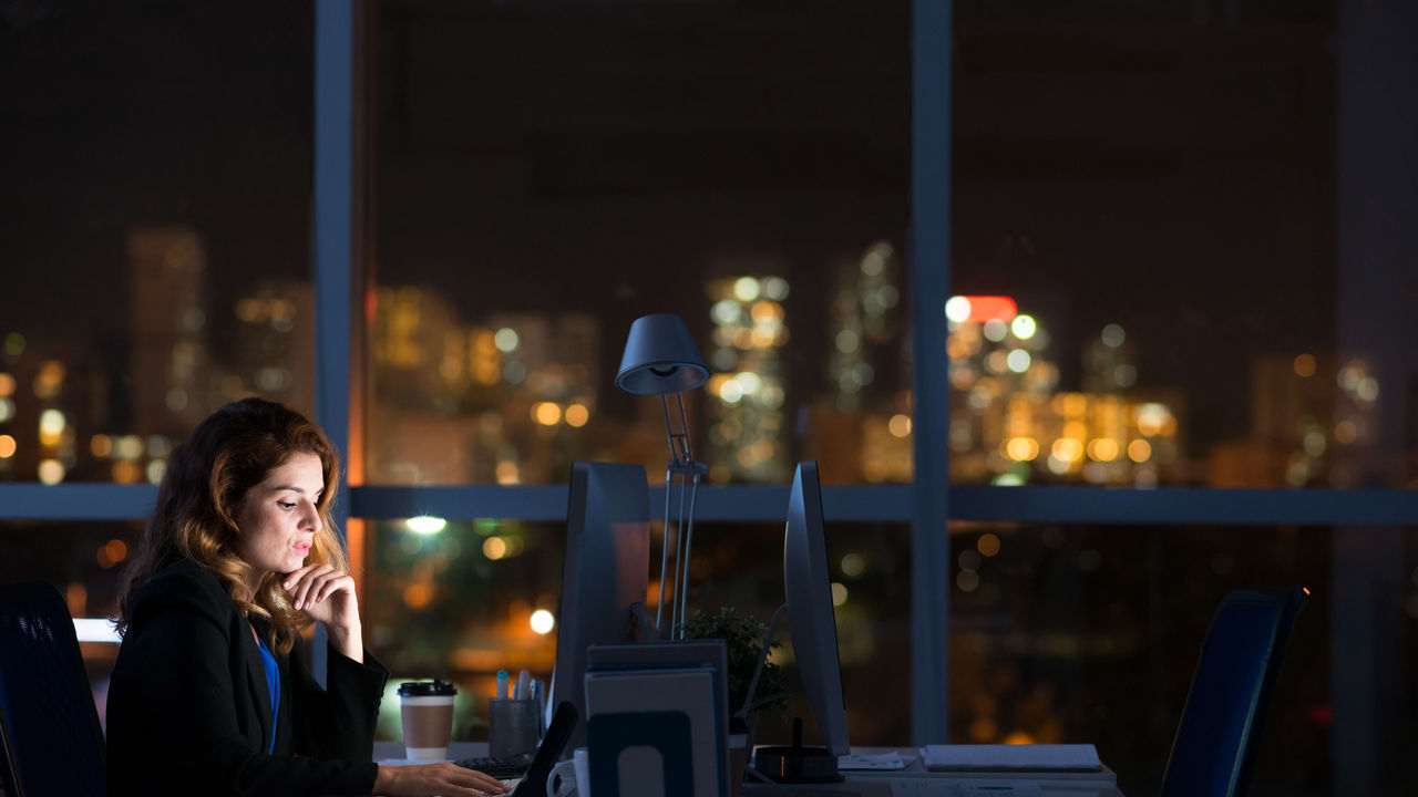 A woman working at a desk at night with a city view.