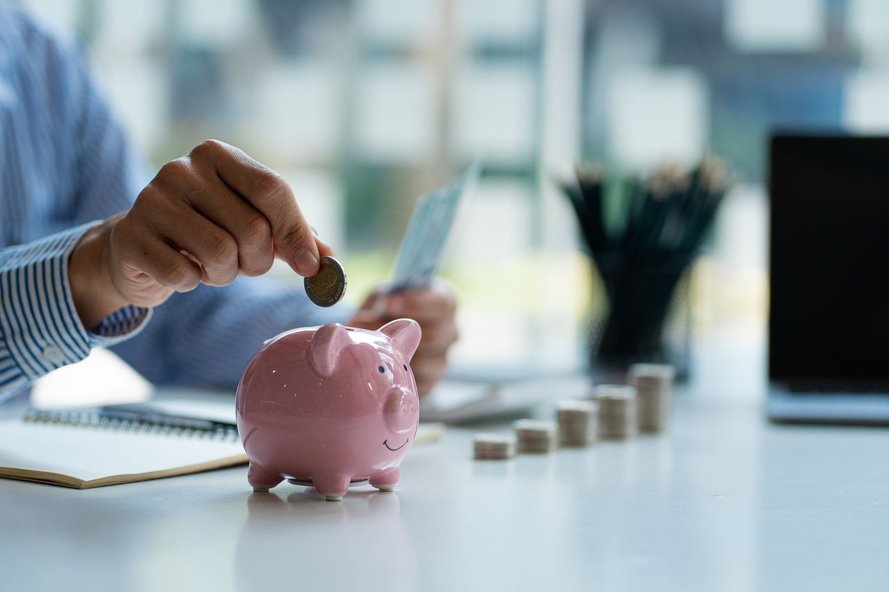 close-up of a person putting money in a piggy bank, indicating retirement savings