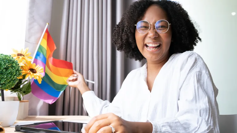 smiling woman works from home next to an LGBTQ pride flag