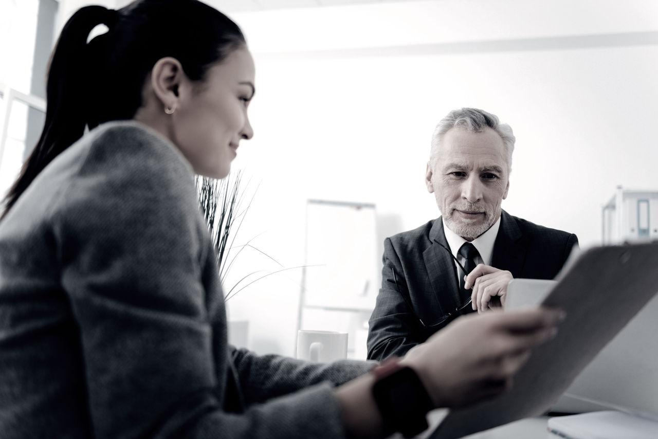 A young woman in professional attire shows an older male executive a tablet.