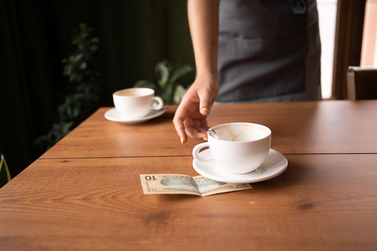 Someone clearing empty coffee cups off a restaurant table, reaching for their tip.