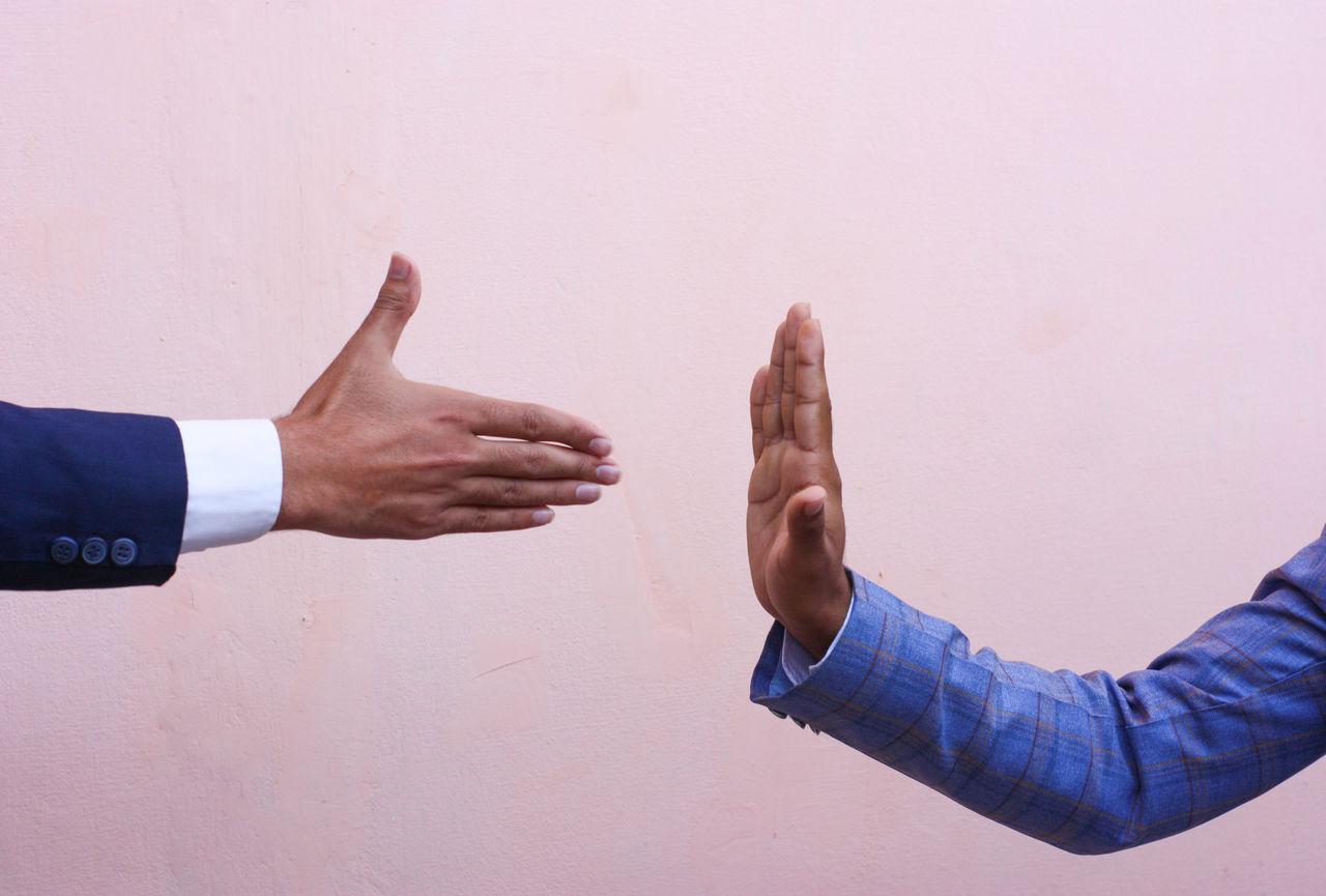 Someone reaching out to shake someone else's hand, but their hand is raised in a motion indicating that they won't shake their hand