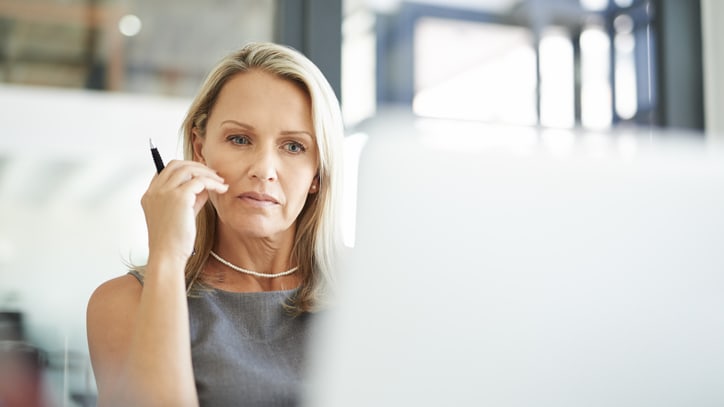 A woman is looking at her phone while sitting in front of a laptop.