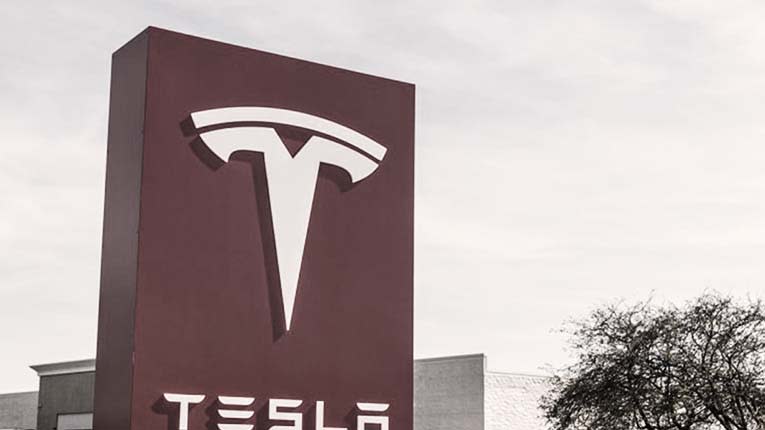 A large Tesla sign with the Tesla logo before a facility.