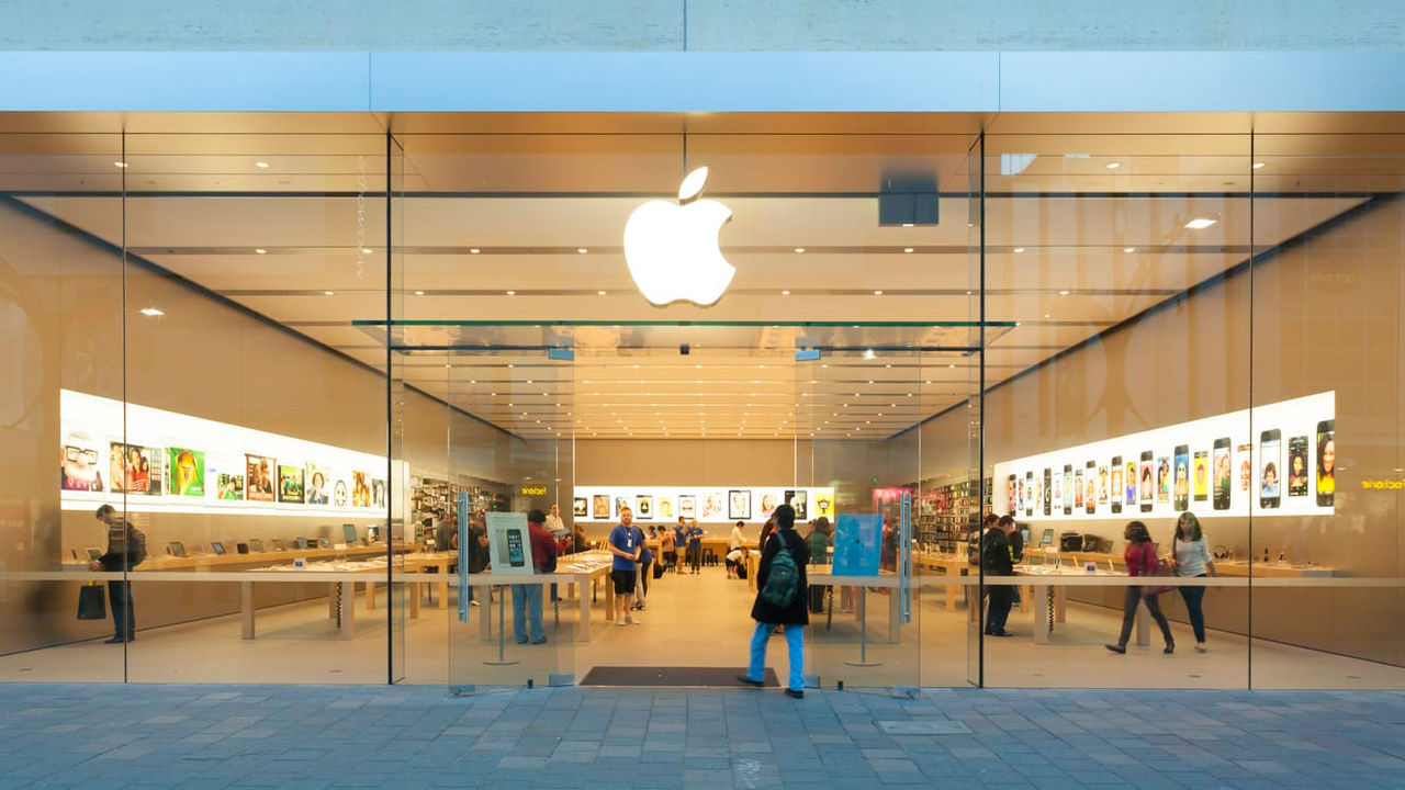 An apple store with people walking in front of it.