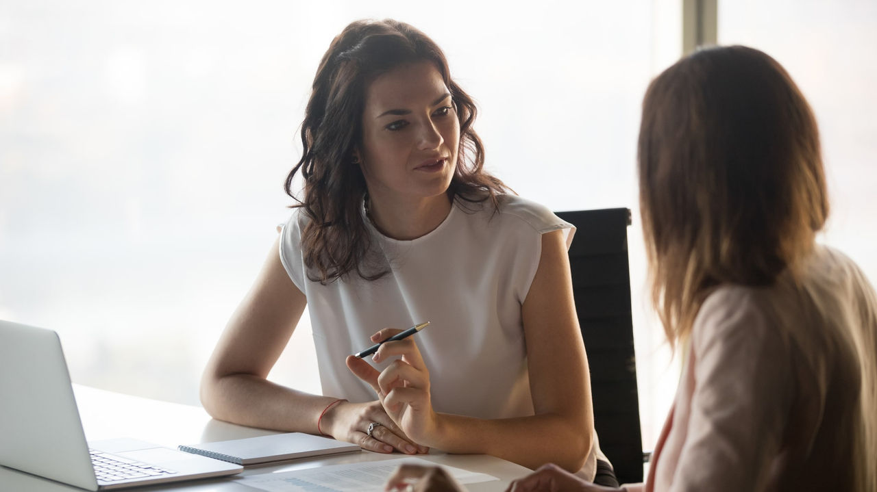 Two business women talking at a table in an office.