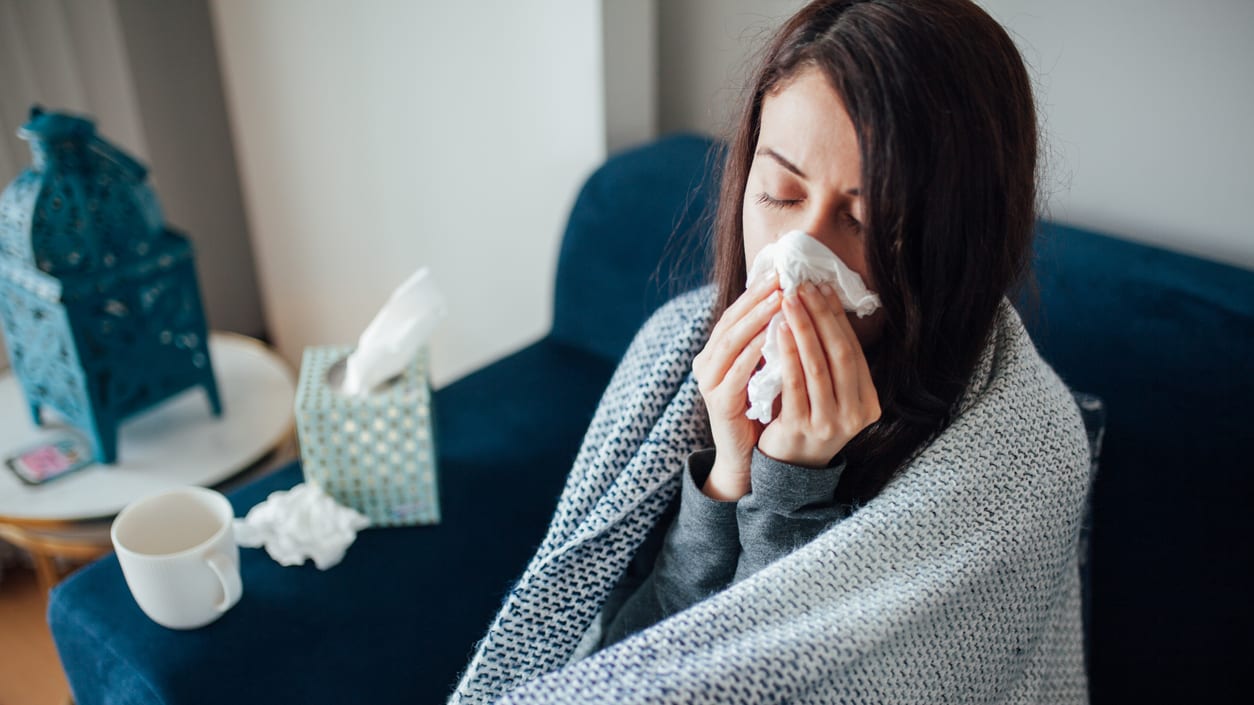 A woman blowing her nose while sitting on a couch.