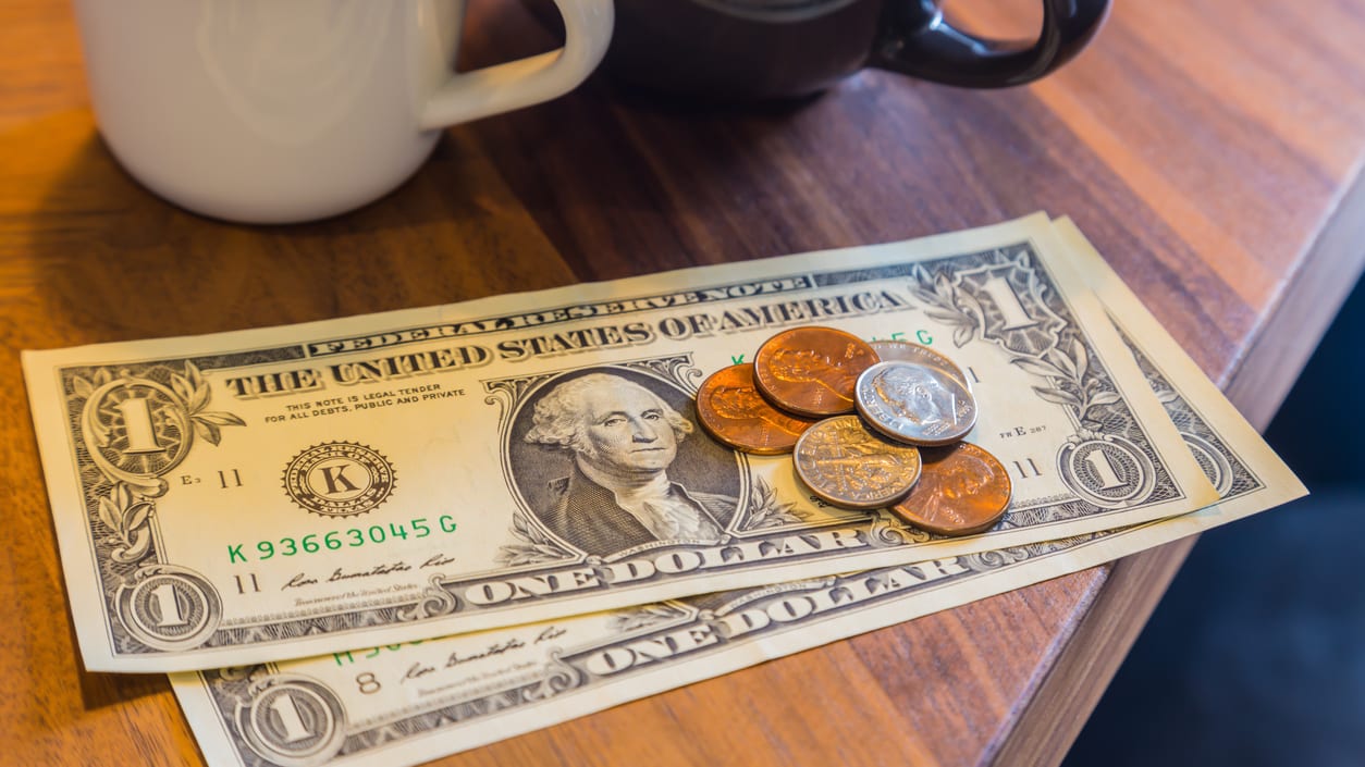 A cup of coffee next to a cup of money.