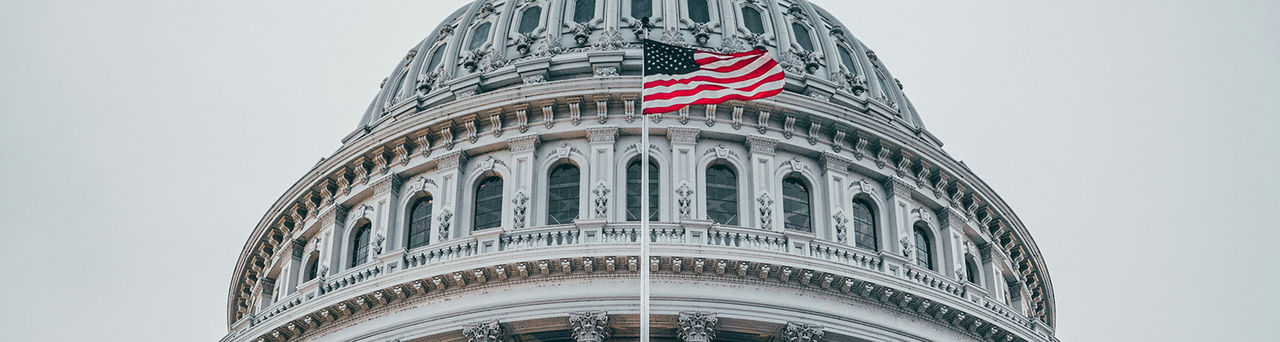 Dome of the U.S. Capitol and the U.S. flag flying before it.