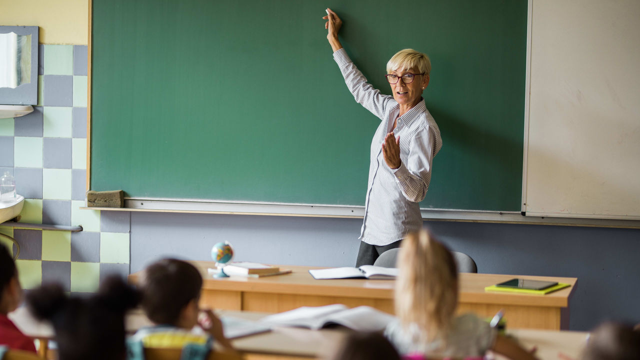 A woman is standing in front of a blackboard with children in front of her.