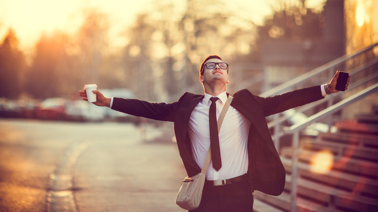 A businessman with his arms outstretched in front of a building.