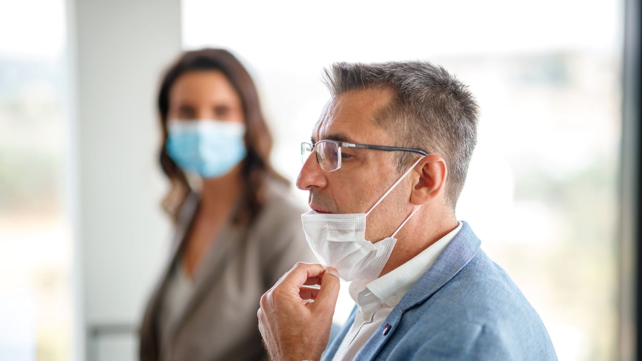 A woman wearing a face mask and a man wearing a surgical mask in an office.