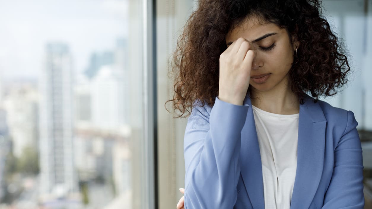 A woman is holding her head in her hands while looking out of a window.