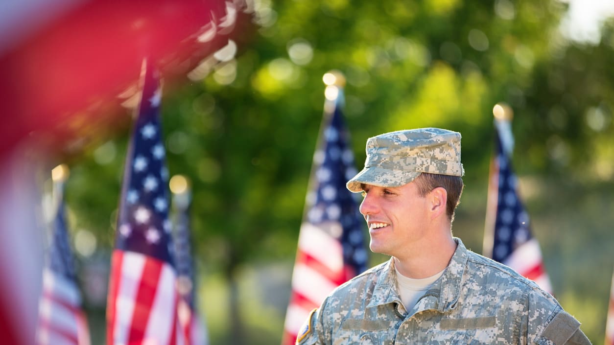A soldier smiles in front of american flags.