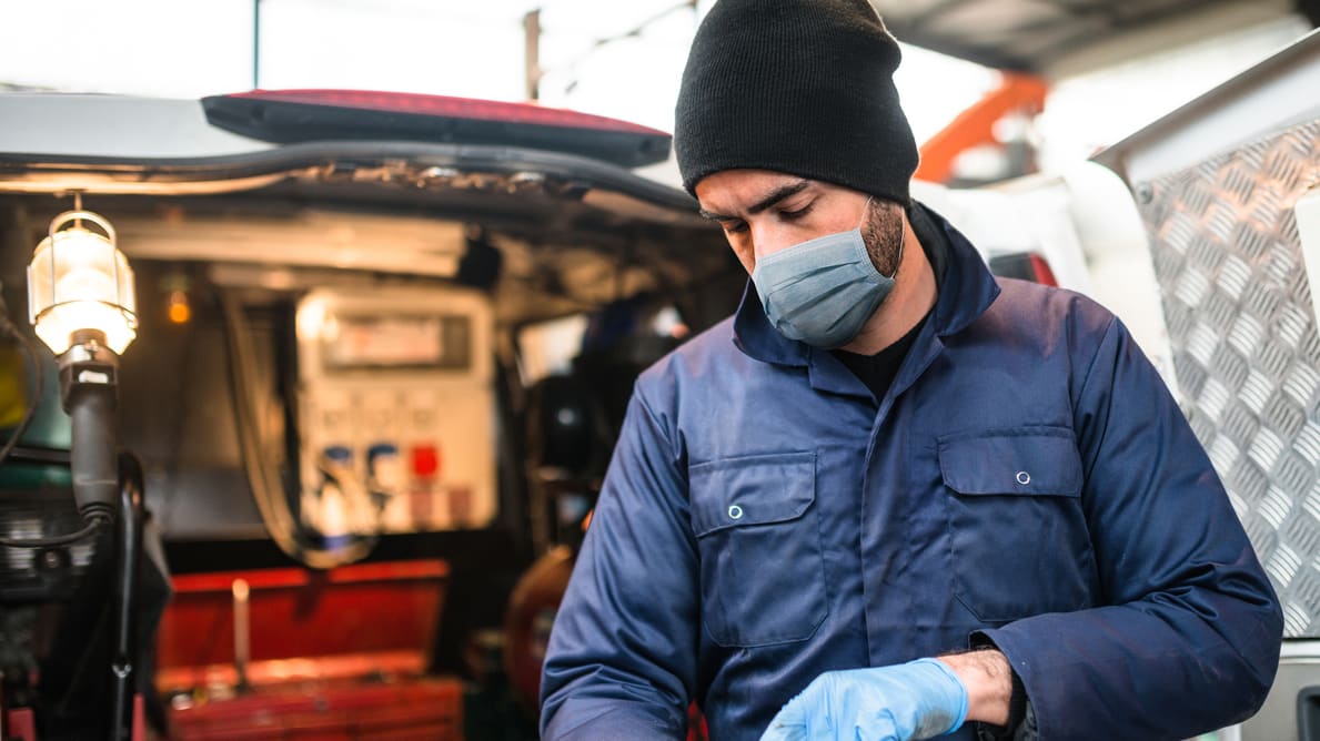 A mechanic wearing a mask and gloves in front of a van.