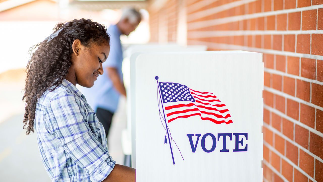 A woman voting in a voting booth with an american flag.