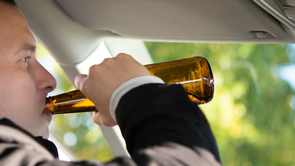 A man drinking from a beer bottle in a car.