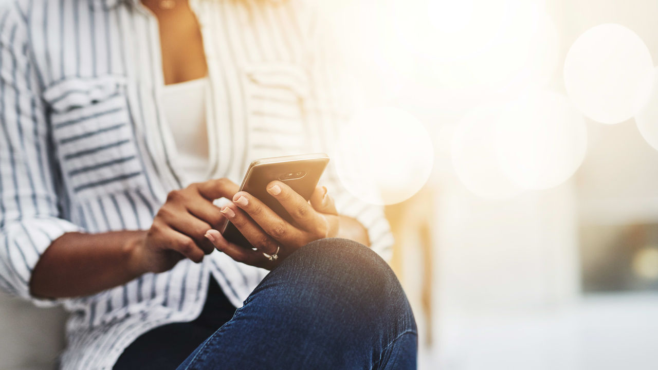 A woman is sitting on a couch and using her cell phone.