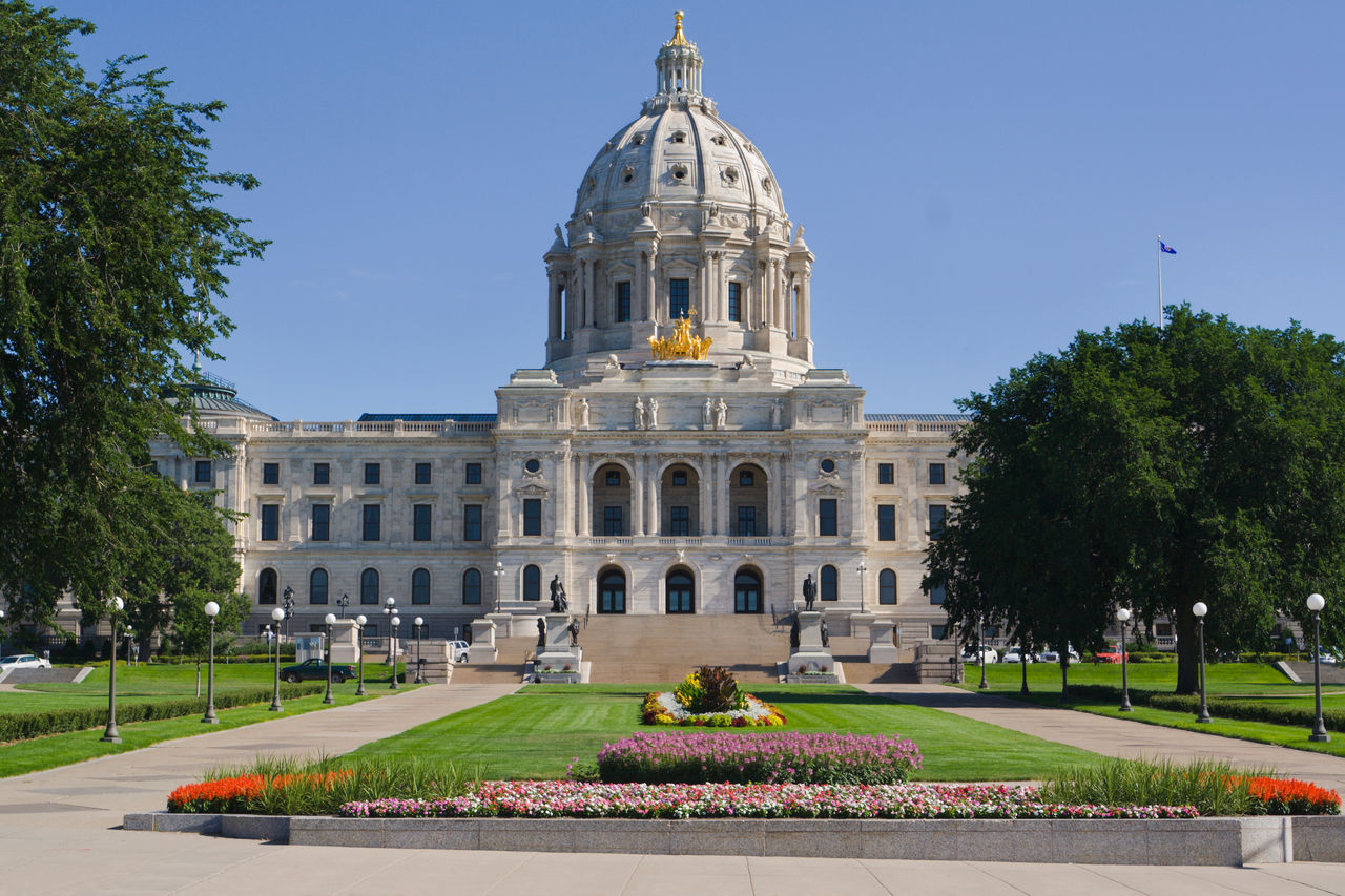 Front entrance approach of the Minnesota State Capitol building in St. Paul, Minn. The architectural classical style of the monumental domed building exterior facade, formal gardens, flower beds, lawns and grounds are a tourist travel destination.