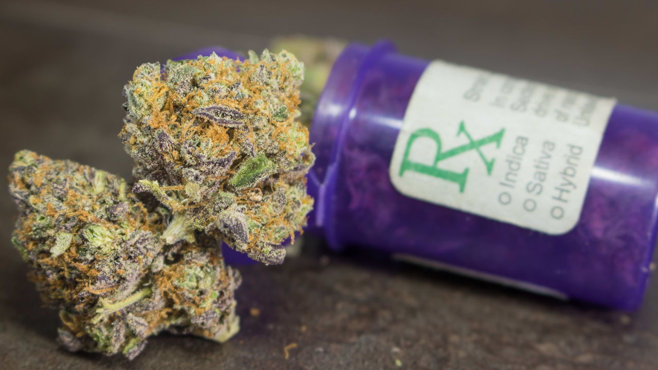 A purple jar with marijuana on top of it.