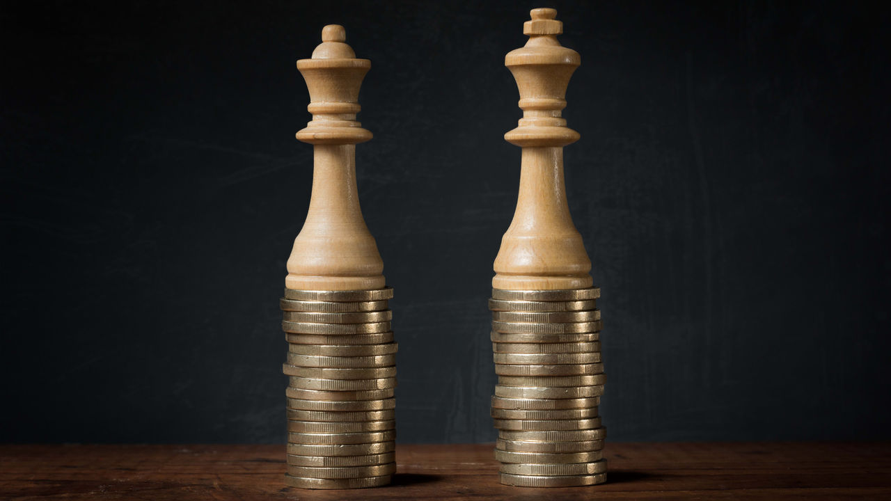 Two wooden chess pawns on a stack of coins.