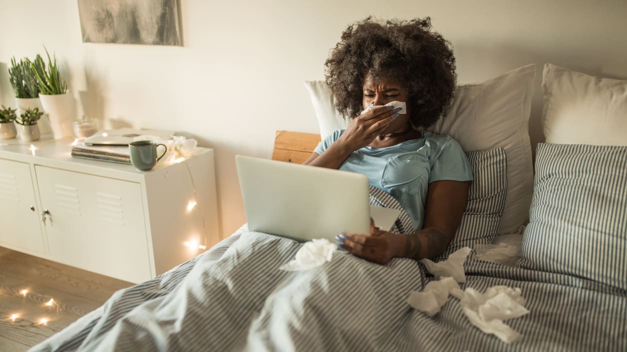 A woman is sitting on her bed with a laptop in her lap.