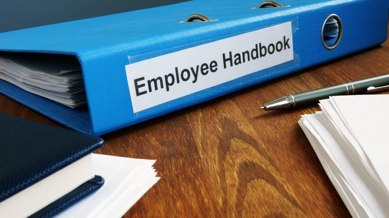 An employee handbook on a desk with a pen.