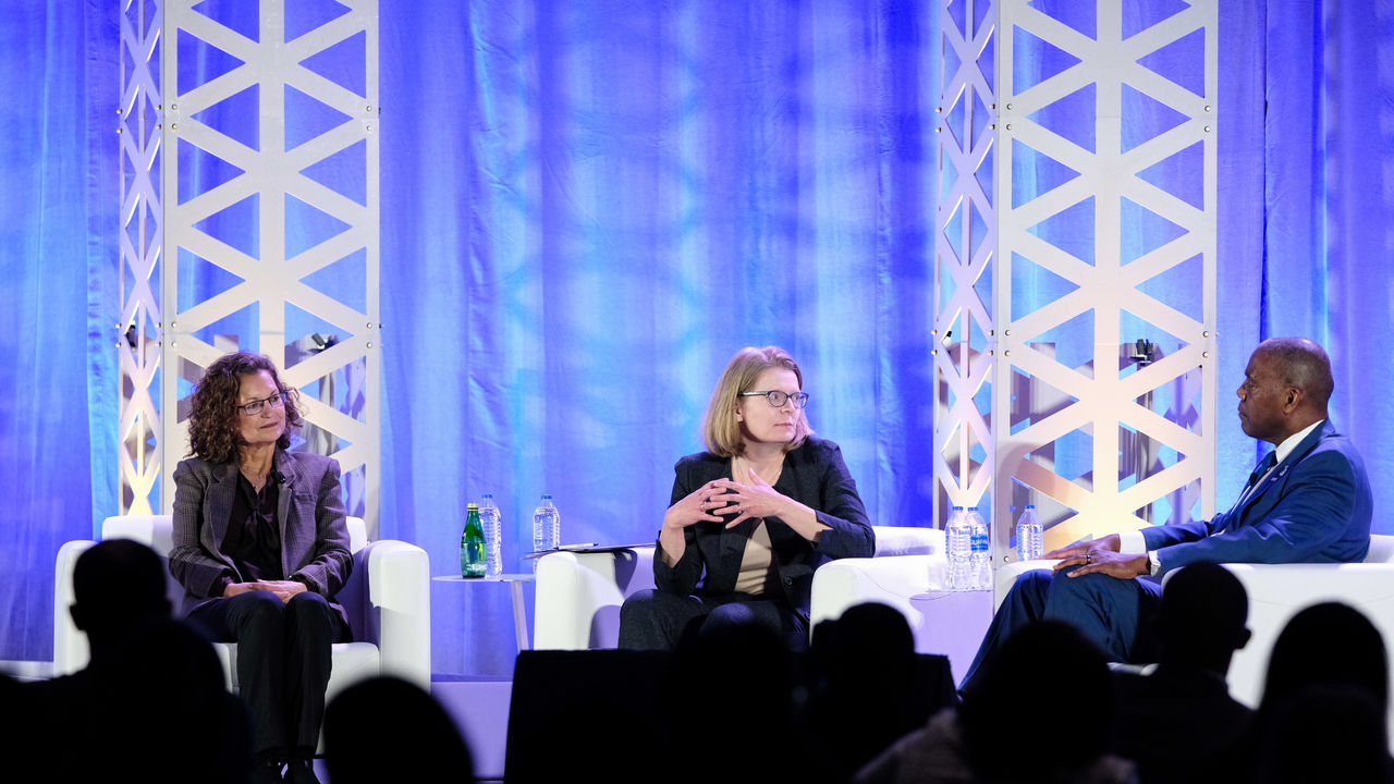 Three women are talking on stage at a conference.