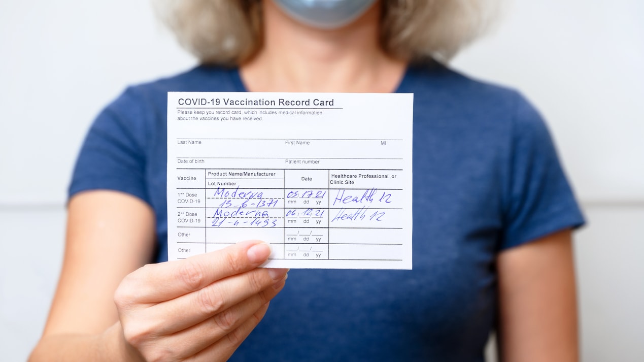 A woman wearing a face mask holding up a coronavirus vaccination form.